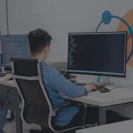 Software developer writing code on multiple computer monitors in a modern office