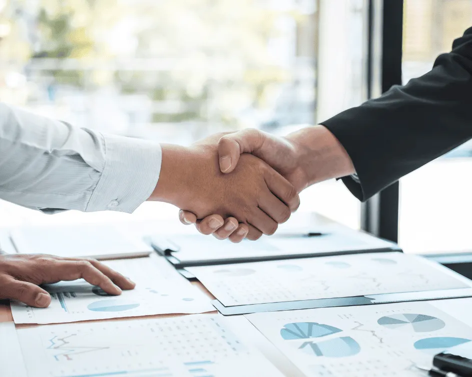 Two business executives shaking hands over financial documents representing client commitment and strategic trust