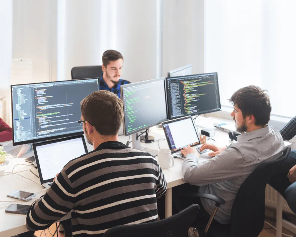 Software developers writing code and monitoring applications on multiple computer screens in an IT development center